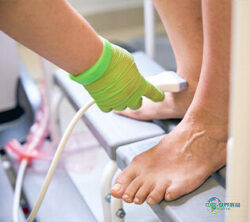 戴绿色手套的手持超声探头检查足部，可见两只裸露小腿；版权：envato